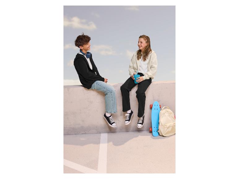 Zwei Teenager sitzen auf einer Mauer, tragen Hoodies, Jeans und Turnschuhe.