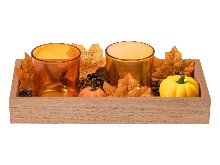 Herbstdekoration mit zwei orangefarbenen Teelichthaltern, Blättern, Tannenzapfen und Kürbissen in einem Holztablett.