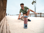 Tragbarer Mixer mit Smoothie auf dem Bürgersteig, mit Mann auf Skateboard im Hintergrund.