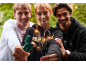 Drei lächelnde Personen halten Wunderkerzen und ein grünes Feuerzeug.