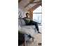 Junge in Kapuzenpullover und Jeans sitzt auf einem grauen Sofa, mit Winterfensterblick.