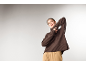 Eine Frau in einem braunen Rollkragenpullover und einer beigen Hose posiert vor hellem Hintergrund.