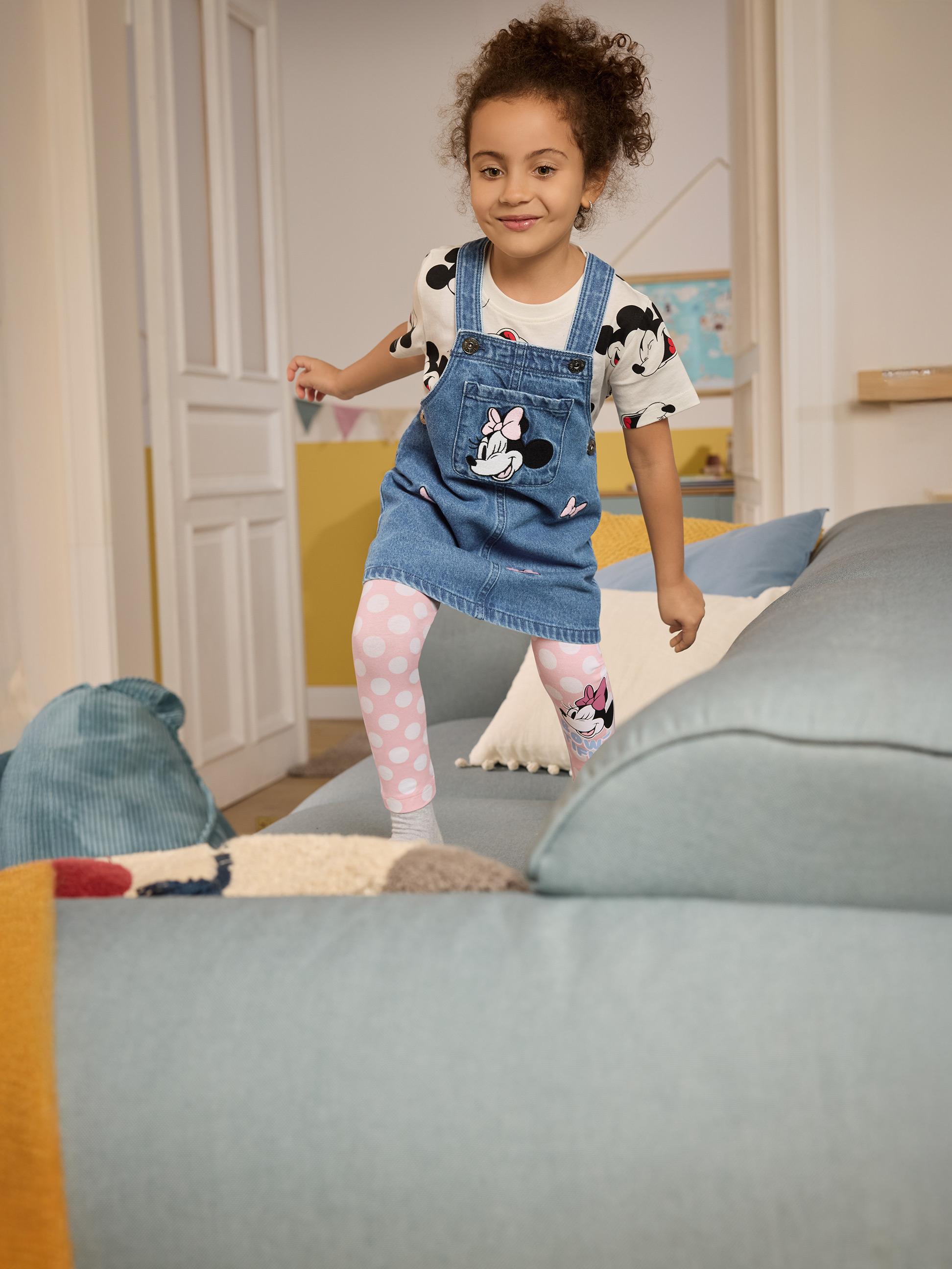 Mädchen in Jeanslatzkleid mit Minnie Maus und rosa gepunkteten Leggings
