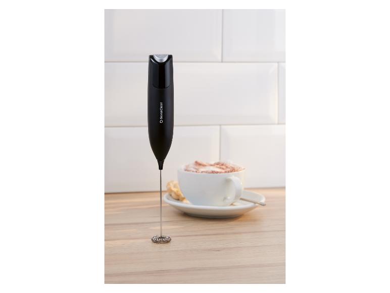 Milchaufschäumer neben einer Tasse Kaffee mit Schaum auf einer Holzoberfläche.