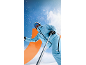 Skifahrer in hellblauer Skijacke und Skihose vor verschneitem Hintergrund.