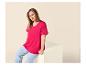 Frau in fuchsiafarbenem T-Shirt und blauen Jeans, sitzt auf einem weißen Block.