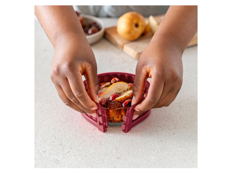 Eine Hand hält eine rote Silikonform mit einem Obstkuchen