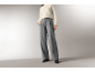 Frau in weißem Strickpullover und grauer, weiter Hose.