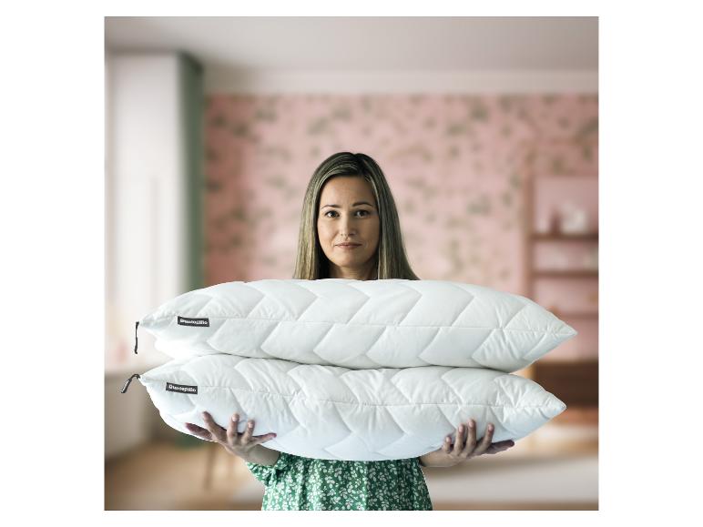 Lächelnde Frau hält zwei weiße gesteppte Dunlopillo Kissen.