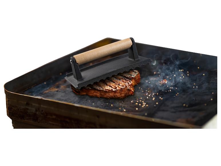 Gegrilltes Steak auf einer Grillplatte mit Steakpresse.