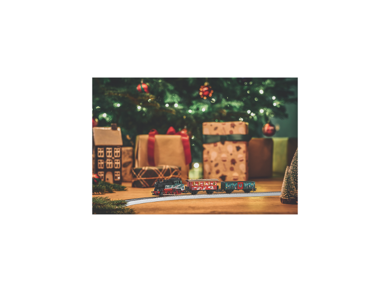 Weihnachts-Spielzeugeisenbahn mit dekorierten Waggons, Geschenken und Weihnachtsbaum im Hintergrund.