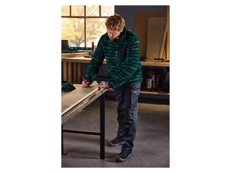Mann in Parkside Arbeitskleidung misst ein Holzbrett in einer Werkstatt.
