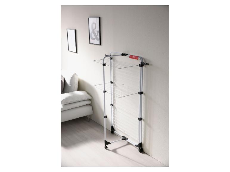 Vertikaler Wäscheständer mit Rollen in einem Wohnzimmer mit Sofa und Bildern.