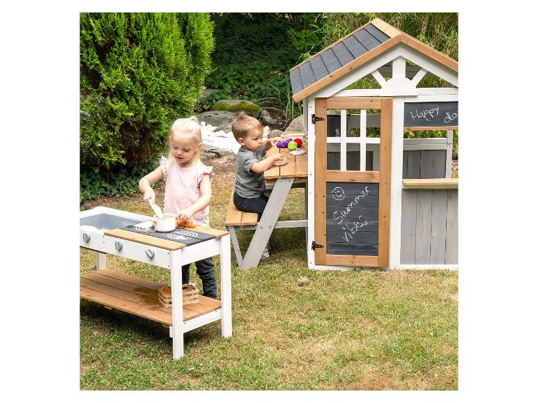 Zwei Kinder spielen mit einer Spielküche und einem Spielhaus im Garten.