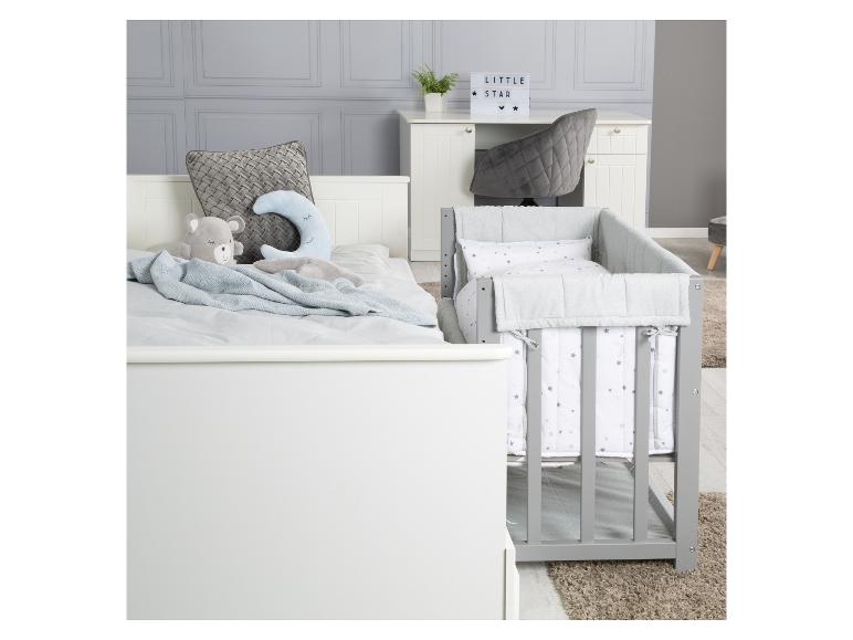 Kinderzimmer mit weißem Bett, grauem Babybett und Schreibtisch mit 'LITTLE STAR' Lampe.