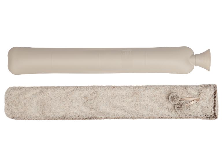 Eine lange beige Wärmflasche und ein flauschiger beiger Bezug mit Pompons.
