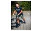 Ein lächelnder Junge in blauem T-Shirt und gemusterten Shorts fährt Roller.