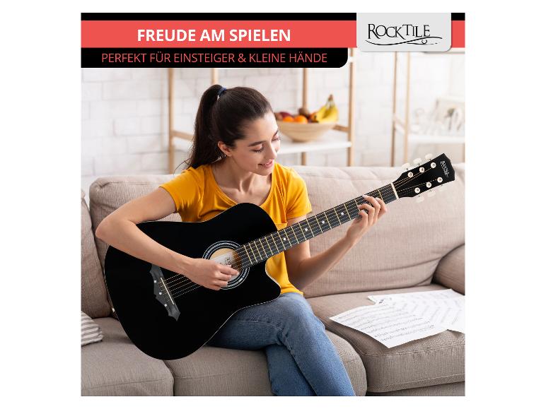 Frau spielt eine schwarze Akustikgitarre auf einem Sofa, mit Noten daneben.