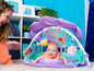 Ein Baby liegt auf einer Spielmatte mit Meerjungfrauen-Motiv mit einem Krabben- und einem Fischspielzeug.