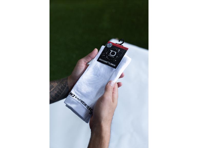 Mann hält weiße Tapedesign Fußballstutzen mit schwarzem Etikett.