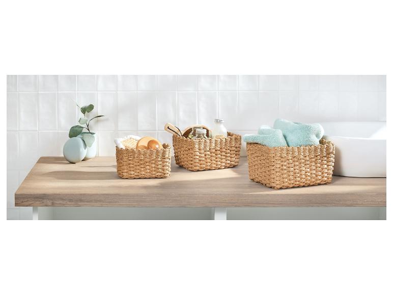 Drei geflochtene Körbe mit Badaccessoires und Handtüchern auf einer Holztheke.
