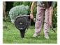 Frau zieht einen Gartenschlauch aus einer automatischen Schlauchtrommel in einem grünen Garten.