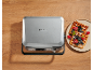 Silbernes Waffeleisen neben einem Teller mit frischen Waffeln mit Beeren auf einem Holztisch.