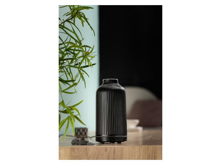 Ein schwarzer keramischer Diffusor für ätherische Öle steht auf einer Holzoberfläche neben einer Pflanze.