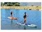 Zwei Personen paddeln auf CRIVIT Allround SUP-Boards auf einem See, umgeben von Hügeln und Bäumen.