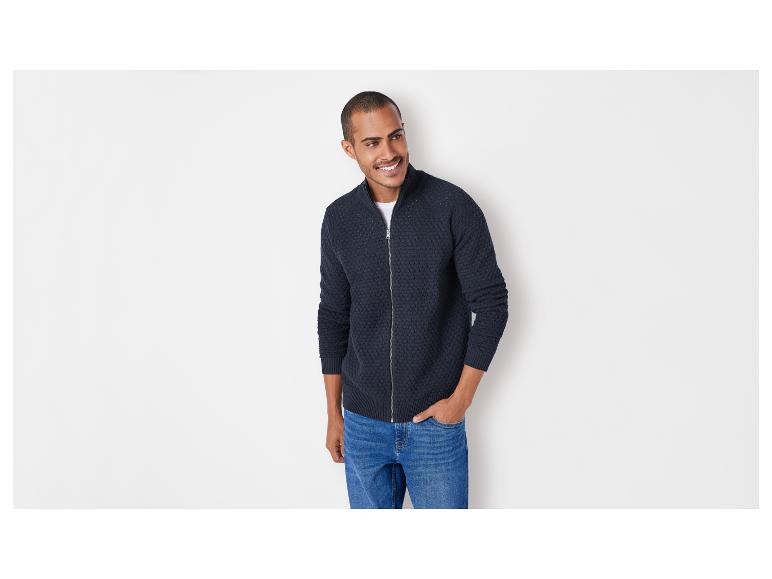 Mann in einem dunkelblauen Pullover mit Reißverschluss und Jeans.