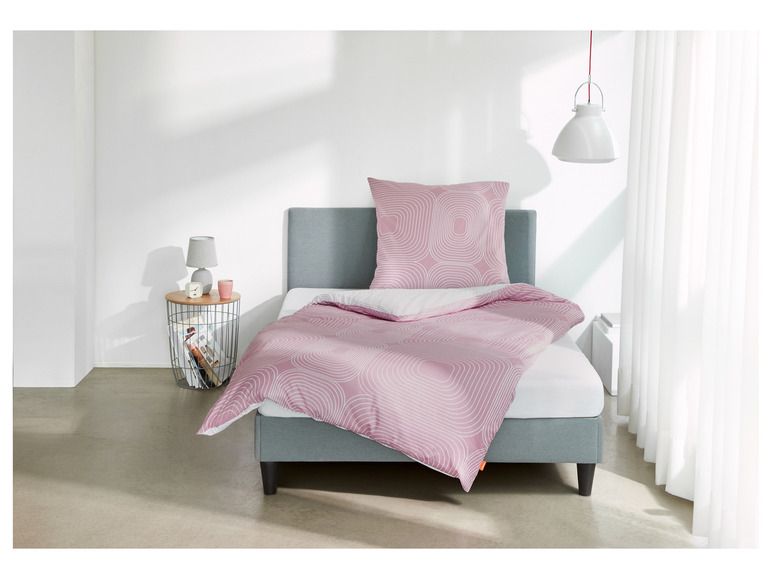 Ein Bett mit einem rosafarbenen Bettbezug mit weißem geometrischem Muster.