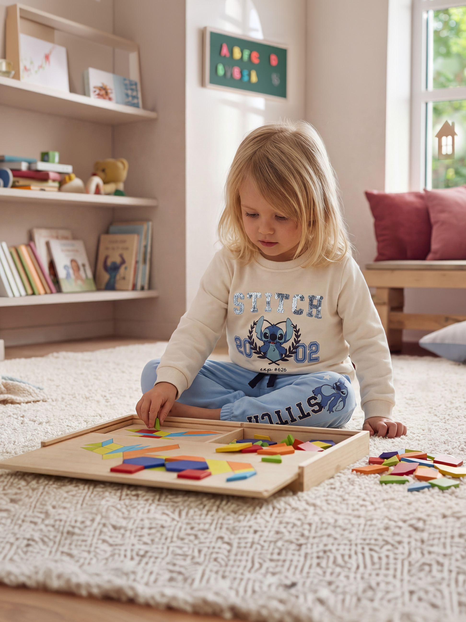 Kind spielt mit einem bunten Holzpuzzle auf einem flauschigen Teppich, trägt Sweatshirt und Jogginghose.
