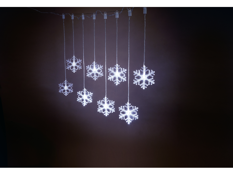 Leuchtende weiße Schneeflockenlichter hängen vor dunklem Hintergrund.