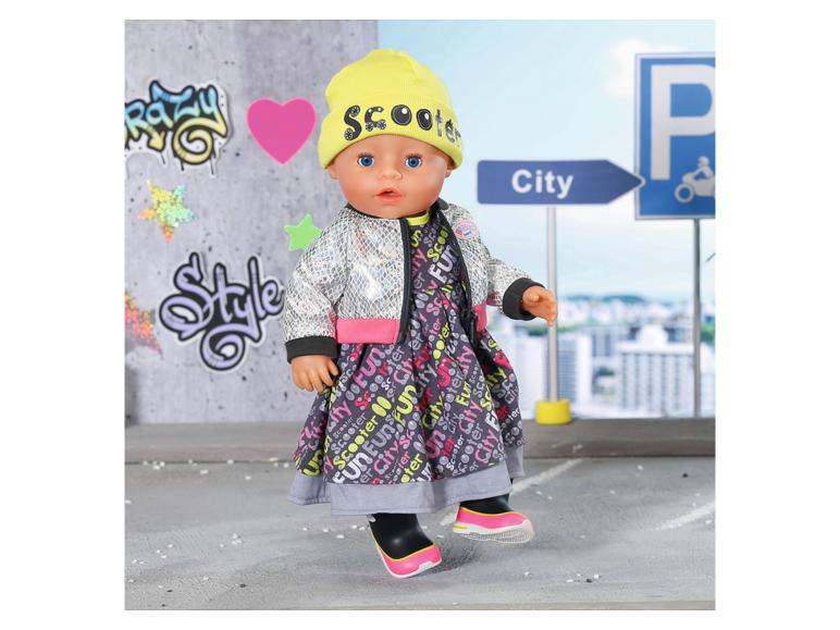 Puppe in einem Kleid mit Stadtmuster, silberner Jacke und gelber Mütze mit der Aufschrift „Scooter“.