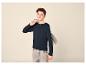 Junge in dunkelblauem Langarmshirt und heller Jeans, mit grauem Kapuzenpullover über der Schulter.