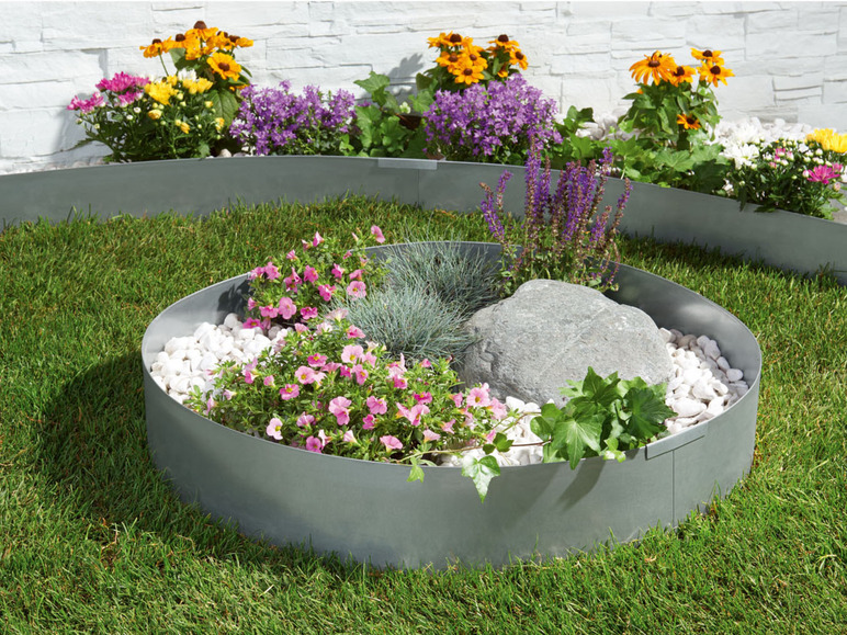 Metallene Gartenbegrenzung mit Blumen und weißen Kieselsteinen.