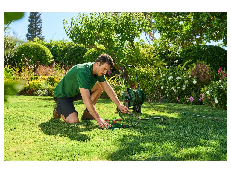 Mann schließt einen Rasensprenger an einen Gartenschlauch auf einem Rasen an.