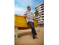 Mann in gestreiftem T-Shirt und dunkler Hose lehnt an einem gelben Boot am Strand.