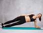 Frau in Sport-BH und Leggings macht einen Plank auf einer blauen Yogamatte.