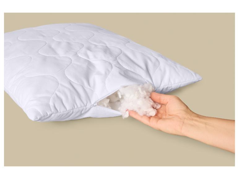 Weißes Kissen mit Reißverschluss, gefüllt mit Fasern, von einer Hand gehalten.
