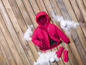 Eine rosa Winterjacke mit Handschuhen auf einem Holzboden mit Schnee.