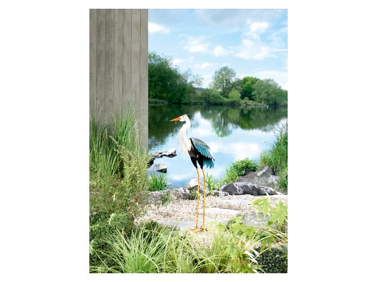 Eine metallene Reiher-Dekoration in einem Garten mit einem Teich.