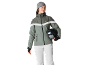 Frau mit grauer Mütze, grüner Skijacke und weißer Hose, hält einen Helm.