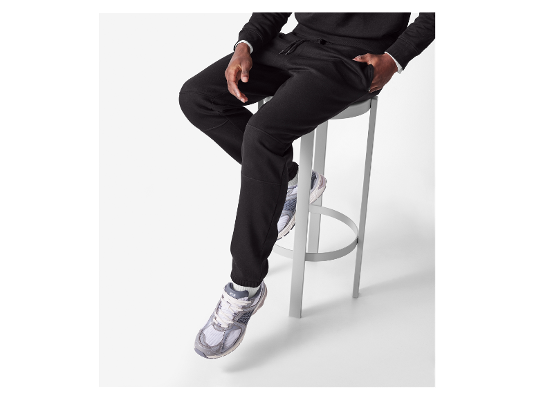 Ein Mann trägt eine schwarze Jogginghose und Sportschuhe.