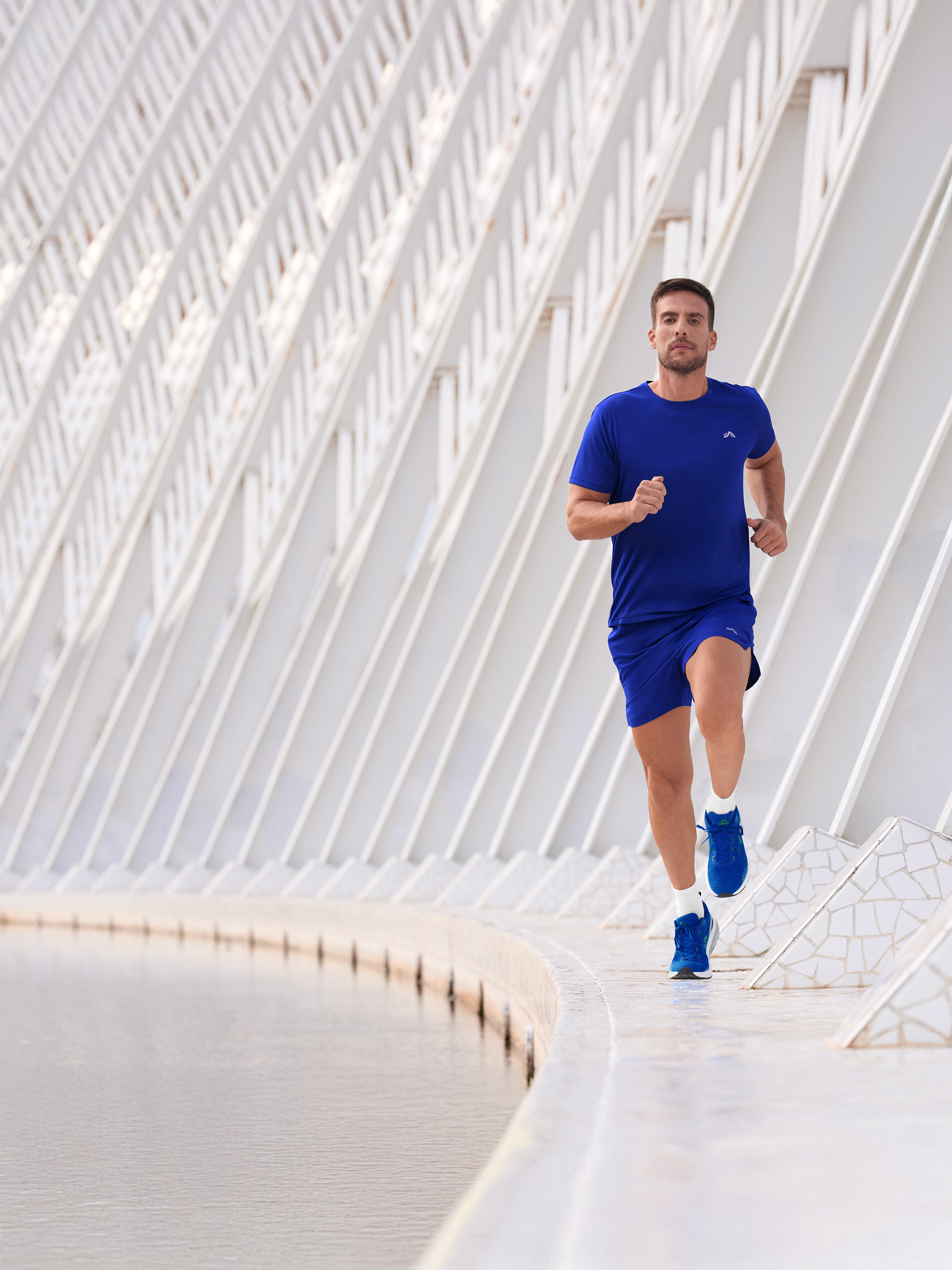 Mann in blauer Sportkleidung, der an einem Gewässer entlangläuft.