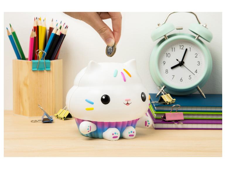Hand steckt Münze in Cupcake-Katzen-Sparschwein, umgeben von Schulmaterial.