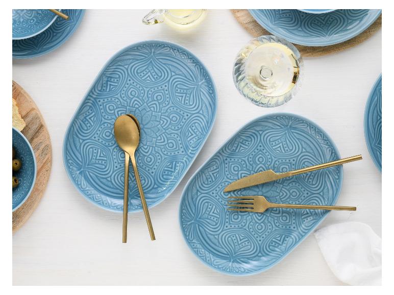 Zwei blaue ovale Teller mit goldenem Besteck.