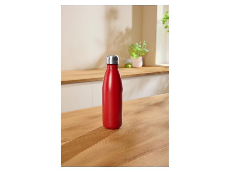 Rote isolierte Wasserflasche auf einer Holzküchenarbeitsplatte mit Pflanzen im Hintergrund.