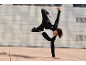 Junger Mann in schwarzem Trainingsanzug und weißem T-Shirt beim Breakdance im Freien.