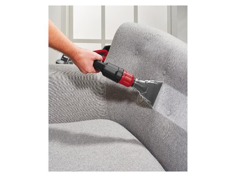 Mann reinigt ein graues Sofa mit einem Polsterreiniger.